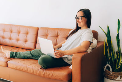 Young smiling brunette woman working on her laptop sitting on the sofa at home