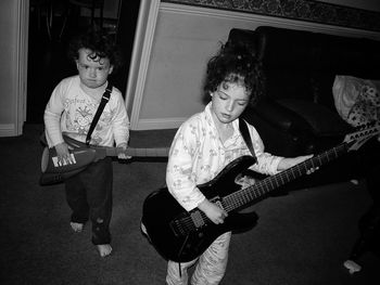 High angle view of siblings playing guitars while standing at home