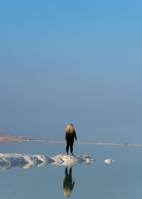 Rear view of woman standing on salt at dead sea against blue sky