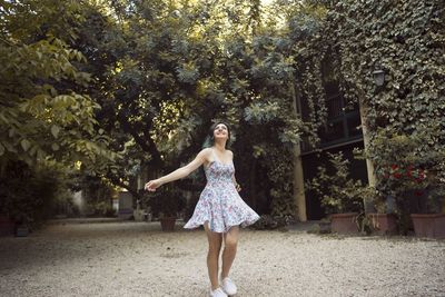 Cheerful young woman in dress spinning against trees