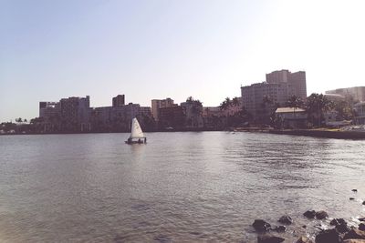 Sailboats in sea by buildings against clear sky