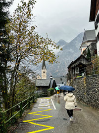 Rear view of woman walking on street of hallstatt lake during rainy gloomy autumn season