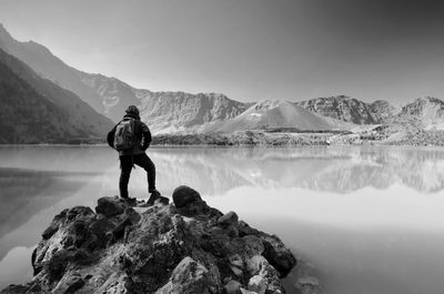 Man standing on rock by lake against sky