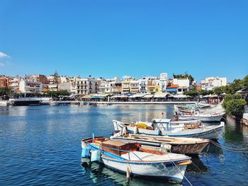 Boats moored at harbor against clear blue sky