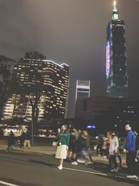 People at illuminated city against sky at night