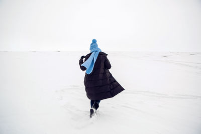 Girl running in a snowy field in a jacket and sunglasses