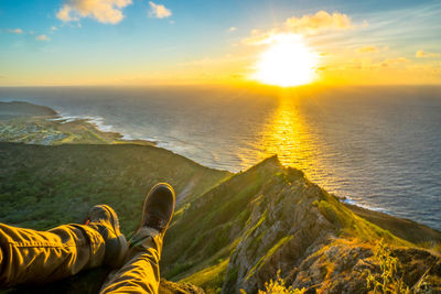 Low section of person by sea against sky during sunset