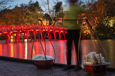 Vietnamese street food vendor in blurred motion against red huc bridge on hoan kiem lake.