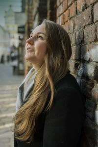 Woman looking up while standing against brick wall