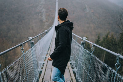 Man standing on footbridge during foggy weather