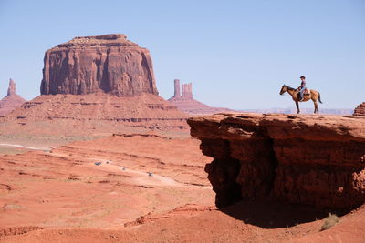 Woman riding horse on mountain against clear sky during sunny day