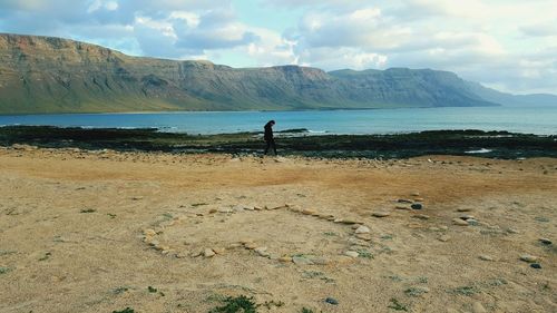 Mid distance view of woman walking on field against mountain