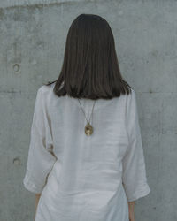 Rear view of young woman wearing chain while standing by wall