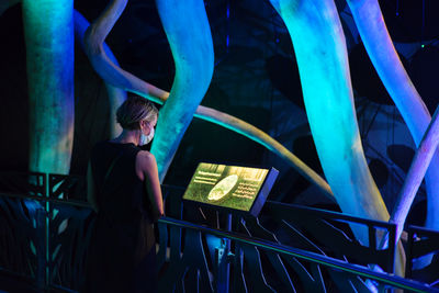 Rear view of woman standing by railing at night