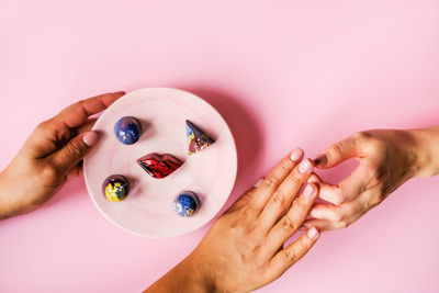Cropped hand of woman holding chocolates in plate while touching hand over pink background