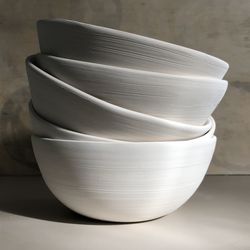 Side angle view of bisque ceramic clay bowls in a stack on table.