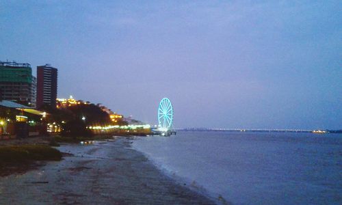 Illuminated city by sea against clear sky at night