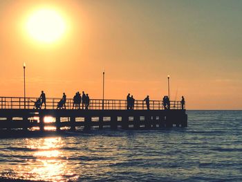 Silhouette people on pier over sea against sky during sunset