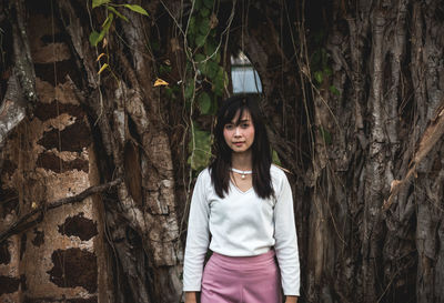 Portrait of woman standing against tree in forest