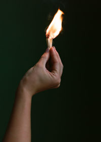 Close-up of hand holding burning matchsticks against black background