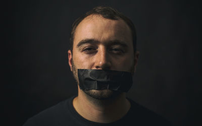 Portrait of man with tape on mouth against black background