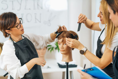 Hairdressers training with mannequin head in education center. professional female hairdresser 