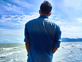 Rear view of man standing at beach against sky