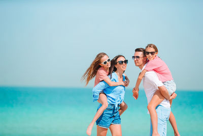 Parents piggybacking daughters at beach