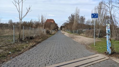 Empty road along plants and trees against sky