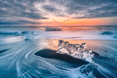 Ice at beach against sky during sunset