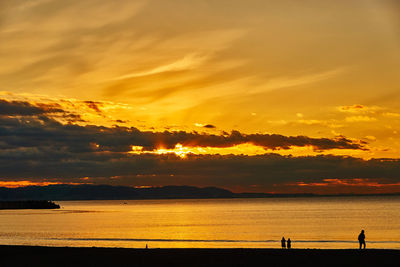 Scenic view of sea silhouette people against sky during sunrise