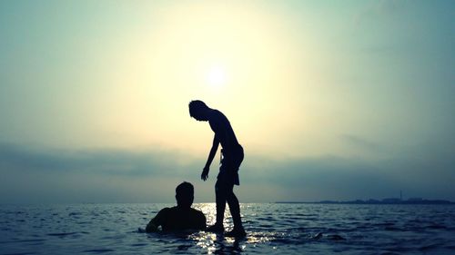 Silhouette people in sea against sky