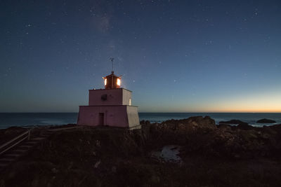 Lighthouse by sea against clear sky at night