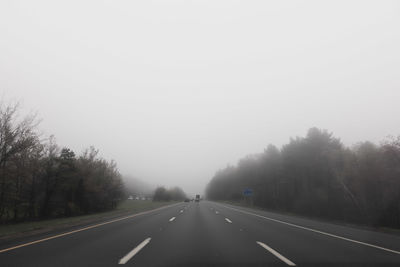 Empty road amidst trees against sky