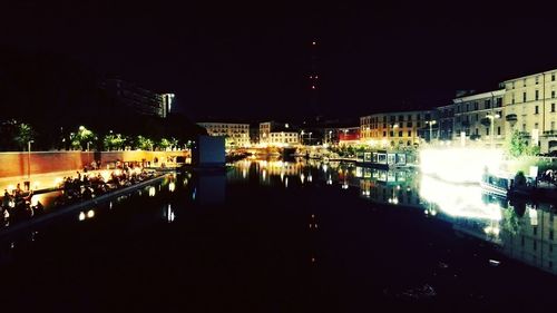 Illuminated city by river against sky at night