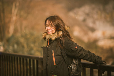 Portrait of smiling young woman standing against railing during winter