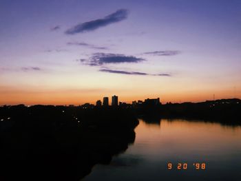 Silhouette of buildings by lake during sunset