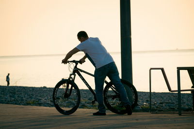 Rear view of man riding bicycle at sunset