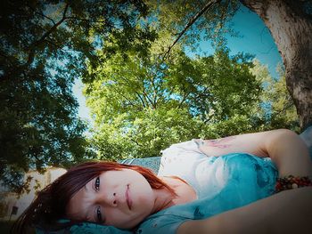 Portrait of woman lying on field against trees at park