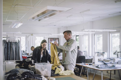Male and female design professionals sorting out recycled clothes while working at workshop
