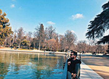 Woman sitting by lake against sky