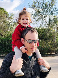 Portrait of happy girl toddler carried by her father against trees and plants