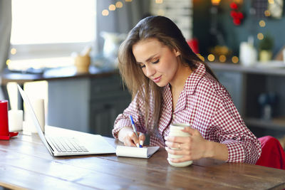 Young woman using phone while sitting on table