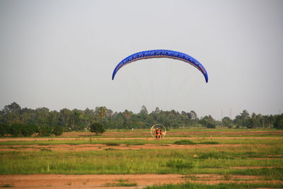 People paragliding on field against clear sky