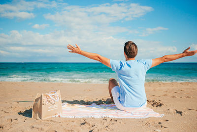 Rear view of woman doing yoga at beach against sky