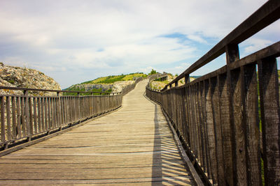 Wooden footbridge on boardwalk against sky