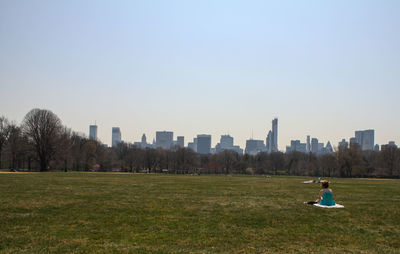 Rear view of man standing on field against cityscape