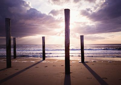 Wooden posts on beach against sky during sunset