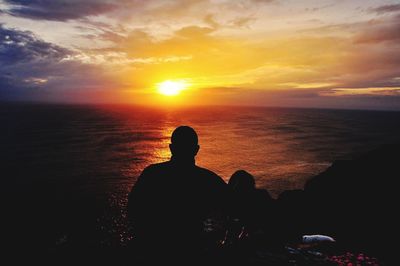 Silhouette man sitting by sea against sky during sunset