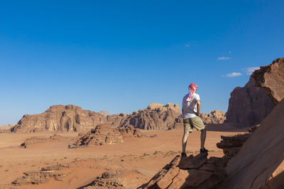 Full length of man standing on rock against blue sky